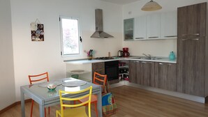 Une cuisine moderne avec des meubles blancs, une cuisinière à gaz et un four encastré. On y trouve une table à manger avec des chaises, et une fenêtre au-dessus.