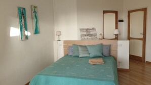 A bedroom with a bed, pillows, a nightstand, a lamp, a mirror, and a door.