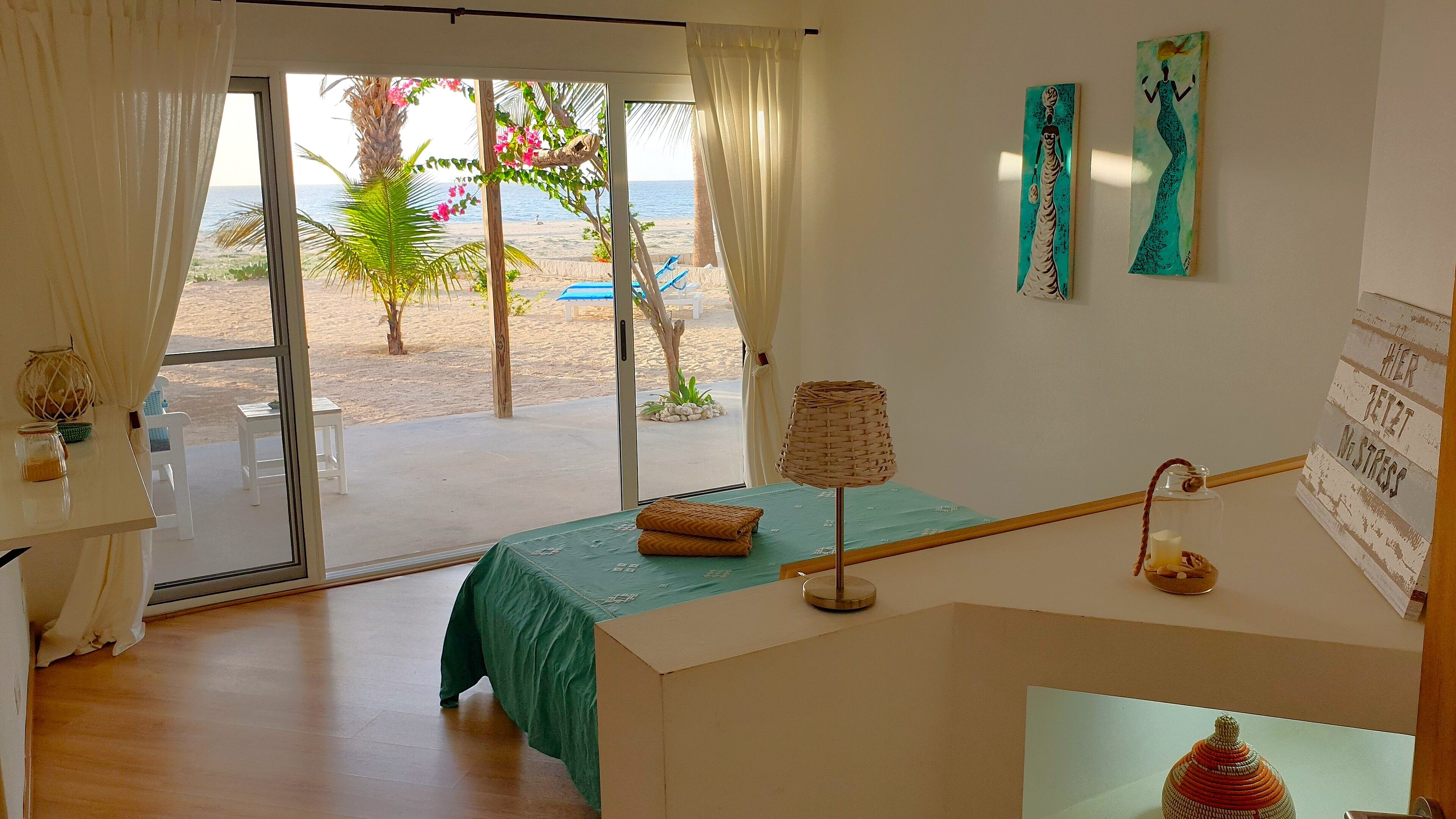 Una habitación con vista a la playa, una cama con cubrecama verde, una lámpara y un letrero con texto.