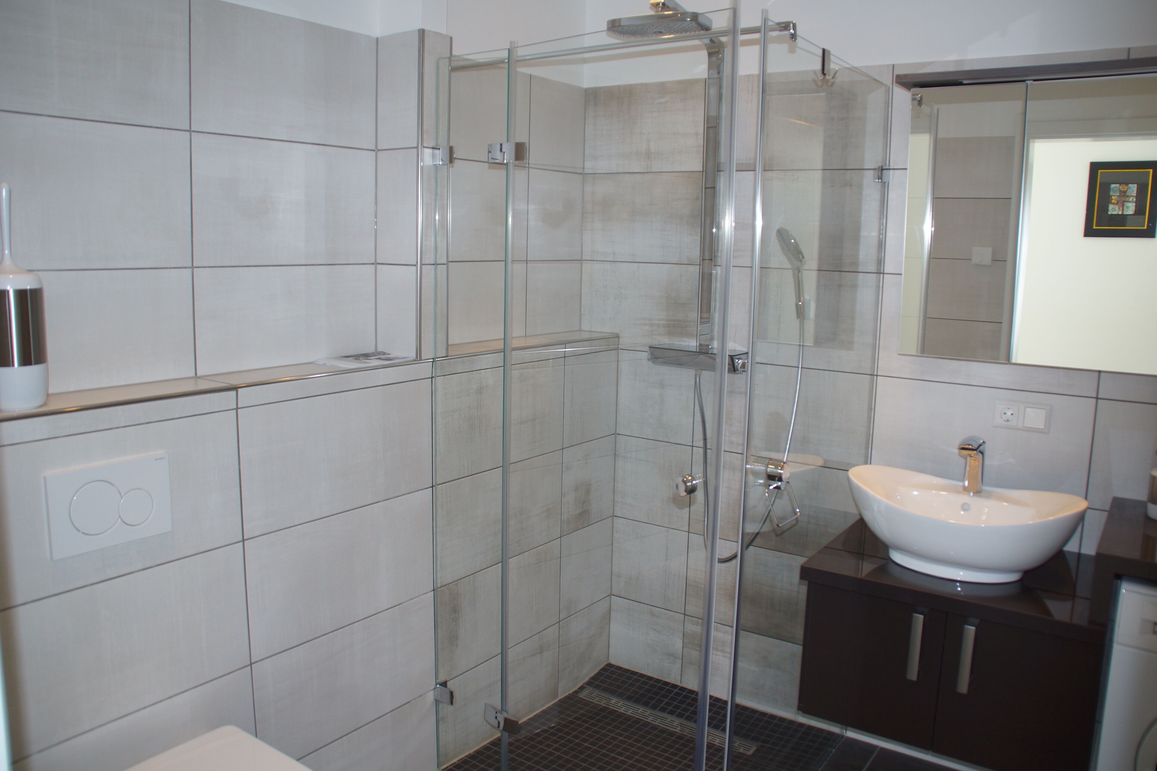 A modern bathroom with a glass shower enclosure, a white sink, and a dark-toned vanity.