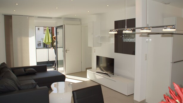 Een moderne woonkamer met een bank, een salontafel en een flatscreen televisie bevestigd aan een wit kastje.