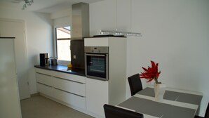 Een moderne keuken met witte kasten, een inbouwoven en een eethoek met een tafel en stoelen.