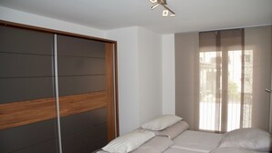 Een slaapkamer met een bed, een houten hoofdeinde en een raam met dunne gordijnen.