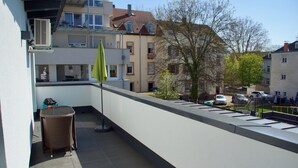 Een balkon met een rieten stoel, een tafel en een groene parasol.