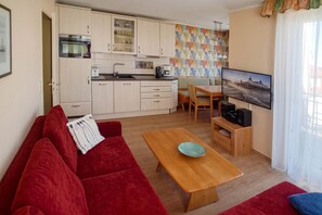 A compact living space with a kitchenette, a red sofa, a wooden table, and a television.