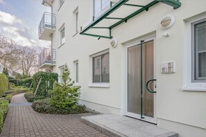 A modern building with a glass door entrance, a small garden area with a pathway, and a metal balcony. - Cozy vacation apartment in Ahlbeck with sea view and balcony on Usedom (Ahlbeck)