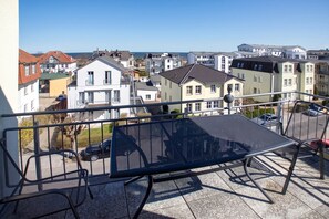 A balcony with a metal table and chairs, overlooking a residential area with various buildings and a clear sky. - Cozy vacation apartment in Ahlbeck with sea view and balcony on Usedom (Ahlbeck)