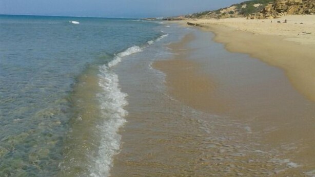 A beach with clear shallow waters, a sandy shore, and rocky cliffs in the background. - Holiday feeling in a quiet area apartment on olive grove with Wi-Fi! (Gonnesa)