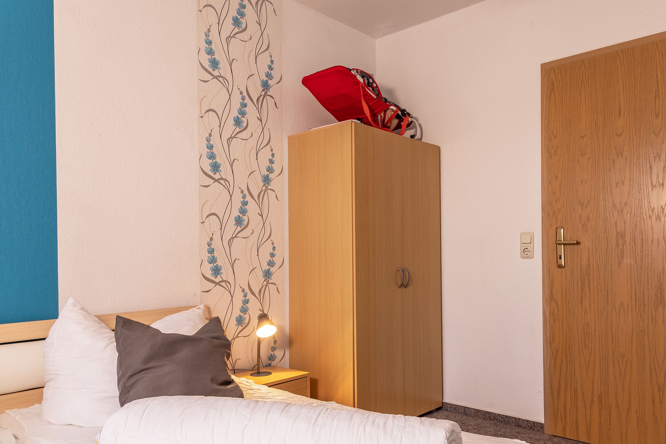 Une chambre à coucher avec un lit, une lampe de chevet, une armoire en bois et une porte.
