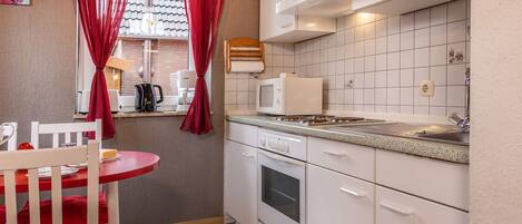 A compact kitchen with white cabinets, a stove, microwave, and a sink.