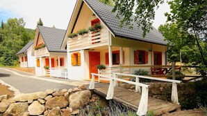A two-story chalet with a stone wall entrance, wooden deck, and a small outdoor seating area. - Cozy cottage house in the idyllic oasis by the stream (Szklarska Poręba)