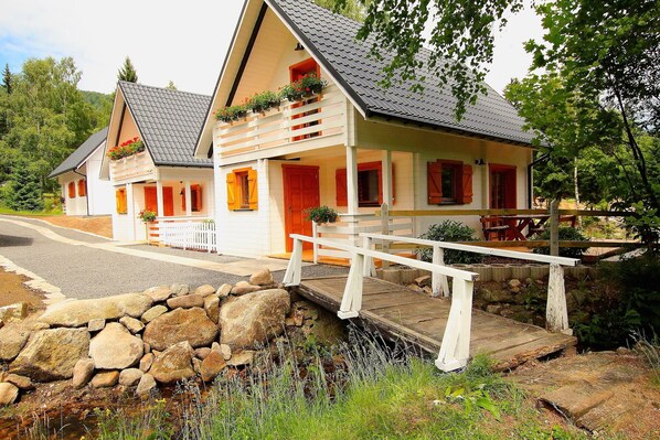 Un chalet de dos pisos con entrada de pared de piedra, terraza de madera y una pequeña zona de estar al aire libre.