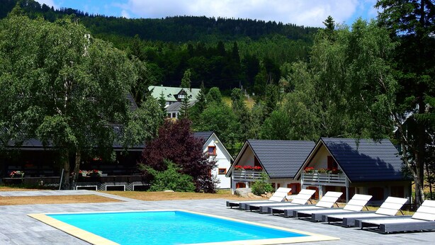 A swimming pool with lounge chairs, surrounded by trees and a mountain in the background. - Cozy cottage house in the idyllic oasis by the stream (Szklarska Poręba)