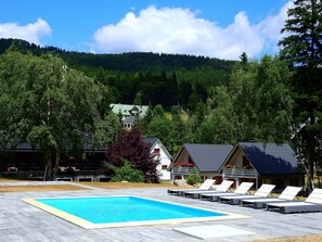 Une piscine entourée de chaises longues, bordée d’arbres et avec une montagne en toile de fond.