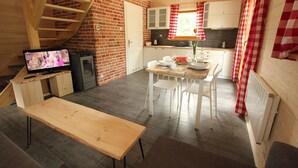 A rustic kitchen with a wooden staircase, a dining table with chairs, and a television on a wooden stand. - Cozy cottage house in the idyllic oasis by the stream (Szklarska Poręba)