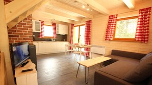A cozy cabin-style room with a wooden interior, a dining area, and a living room with a sofa and a TV on a wooden stand. - Cozy cottage house in the idyllic oasis by the stream (Szklarska Poręba)