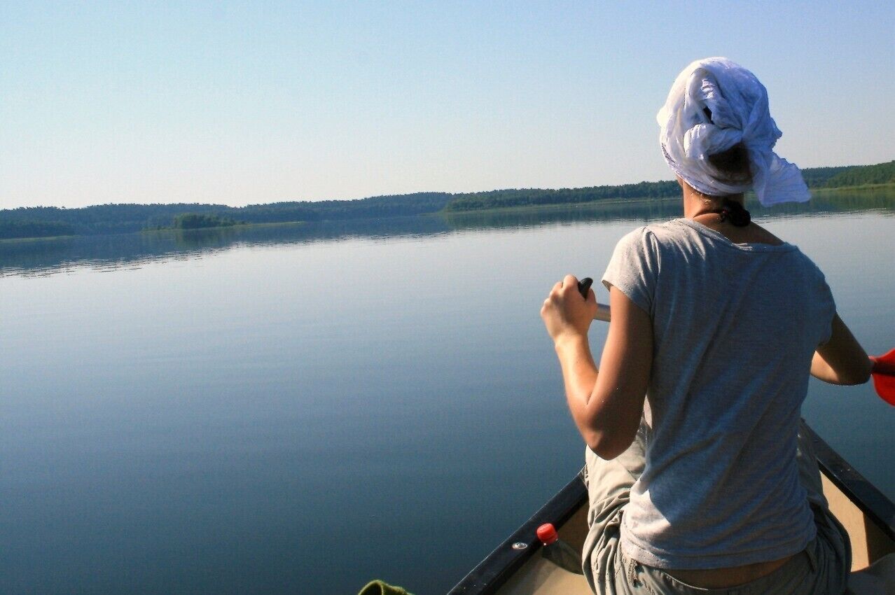 Una persona en un bote sobre un lago tranquilo con una orilla boscosa al fondo.
