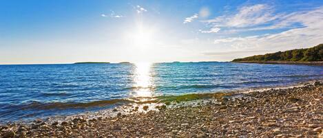 A pebbled beach with calm waters and a clear sky.