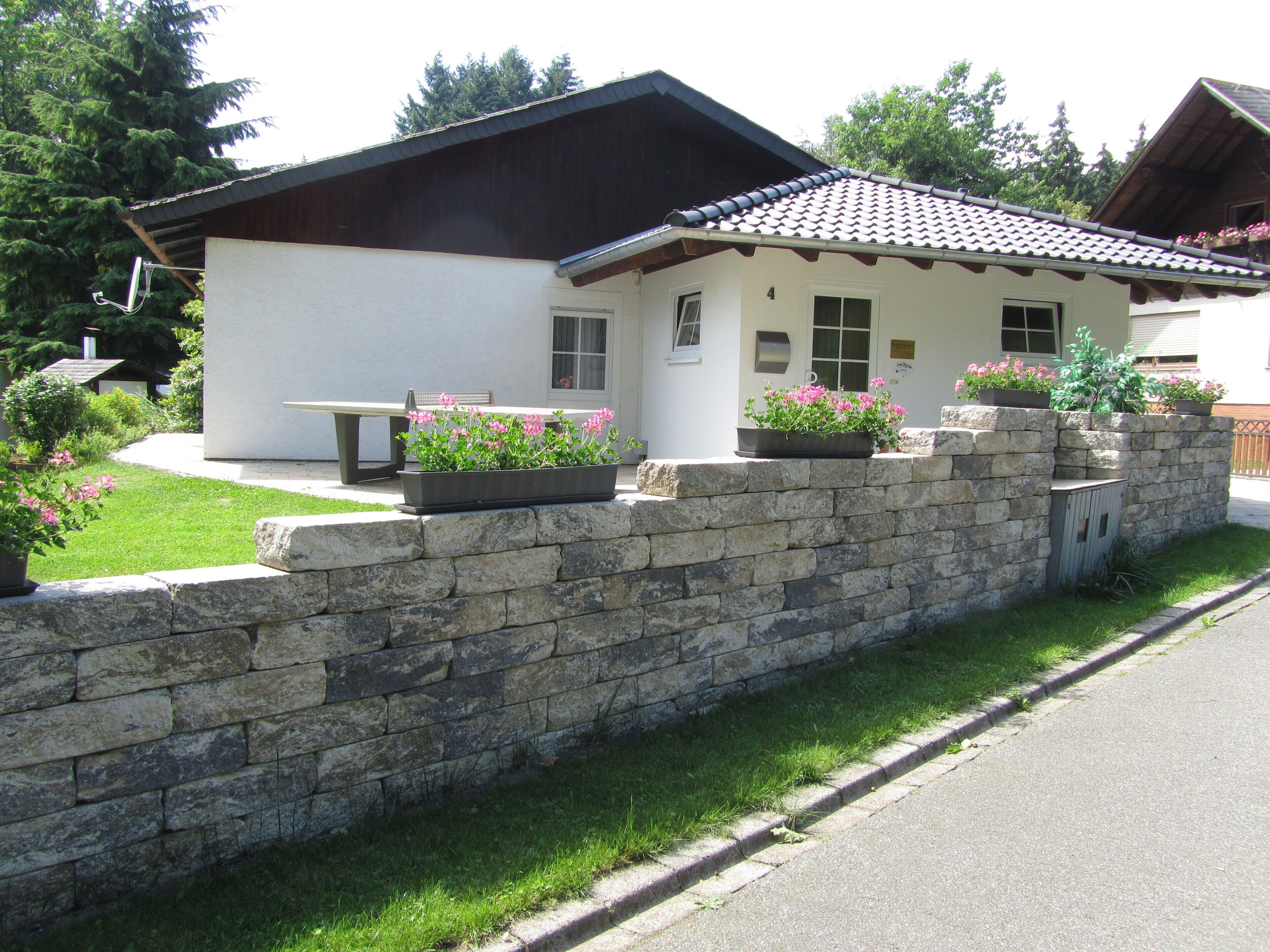 Ein Haus mit einer Steinsäule, einer Terrasse mit einer Bank und Blumenkästen.