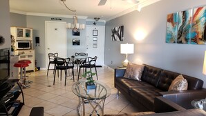 A modern living room with a glass coffee table, a brown leather sofa, and a dining area with a glass table and chairs. -  Condo/apt. near Disney, Universal, 3 pools, WIFI,free Parking !  (Florida)