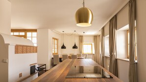 Ein moderner Essbereich mit einem langen Holztisch, Pendelleuchten und einem großen Fenster mit Vorhängen.
