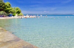 A beach with clear water, a pier, and boats.