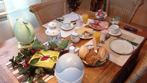Une table à manger dressée avec des assiettes, des tasses, un saladier de fruits et une bouteille de jus d’orange.
