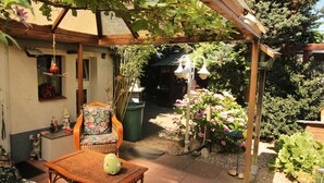 Un patio couvert comprenant une chaise en osier, une table et une mangeoire à oiseaux suspendue.