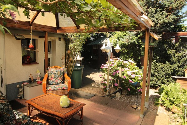 Un espacio de patio techado con una silla de mimbre, una mesa y un comedero colgante para pájaros.