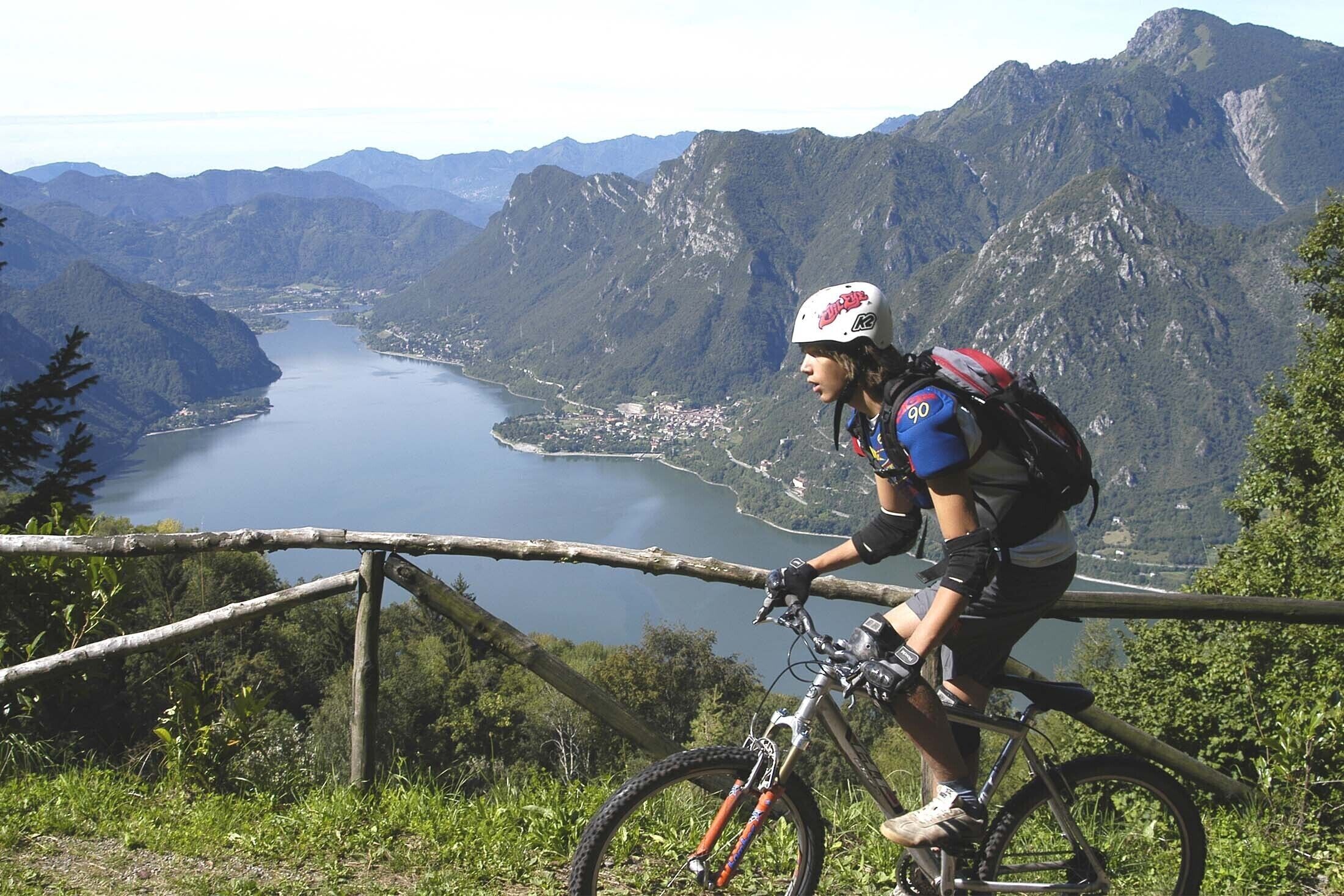 Un ciclista de muntanya a un sender amb una vista panoràmica d'un llac i muntanyes.