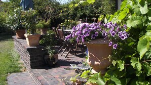 Un patio con pared de ladrillo, plantas en macetas y una mesa con sillas.
