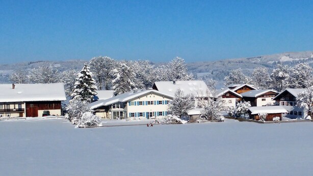 A snow-covered village with traditional wooden houses, a large building with blue windows, and a mountain backdrop. - Luxury Vacation Apartment (160 sqm) near Neuschwanstein (Schwangau)