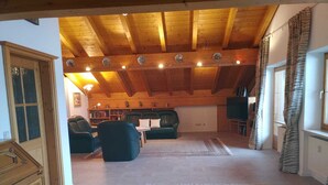 A spacious living area with a high wooden ceiling, a fireplace, a sofa, a coffee table, and a television. - Luxury Vacation Apartment (160 sqm) near Neuschwanstein (Schwangau)