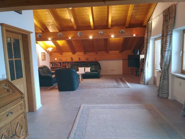 Amplia sala de estar con un techo alto de madera, una chimenea, un sofá, una mesa de centro y un televisor.