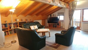 A cozy living room with a leather sofa, a coffee table, and a TV. There are bookshelves filled with books and decorative items. - Luxury Vacation Apartment (160 sqm) near Neuschwanstein (Schwangau)