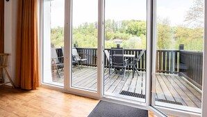 Una habitación con un amplio ventanal corredero que da a una terraza exterior con una mesa y sillas.