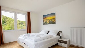 Un dormitorio con cama, mesita de noche, lámpara, ventana con cortinas y un cuadro de girasoles.