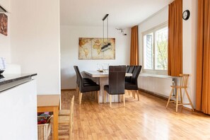 Een eetruimte met een houten vloer, een witte tafel, zwarte stoelen en een groot abstract schilderij aan de muur.