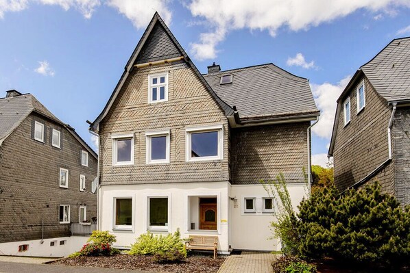 Een woonhuis met twee verdiepingen, een puntige dakschildering, een voortuin en een kleine tuin.