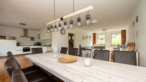 Una cocina moderna con una mesa larga de comedor, varias sillas e iluminación colgante.