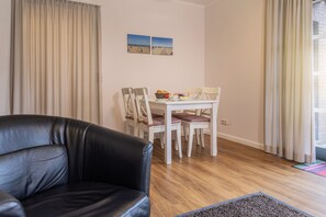 Ein Wohnzimmer mit einer schwarzen Ledersofa, einem weißen Esstisch mit Stühlen und einem Fenster mit Vorhängen.