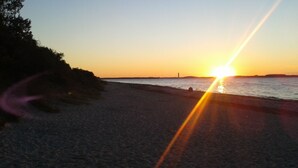 Une plage au coucher du soleil, le soleil étant bas à l’horizon, projetant une lumière dorée sur l’eau et le sable.
