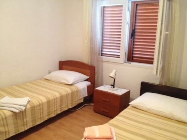 A small, clean room with two single beds, a nightstand with a lamp, and a window with blinds. - Holiday Home in Sali with Seaview, Terrace (4420-1) (Sali)