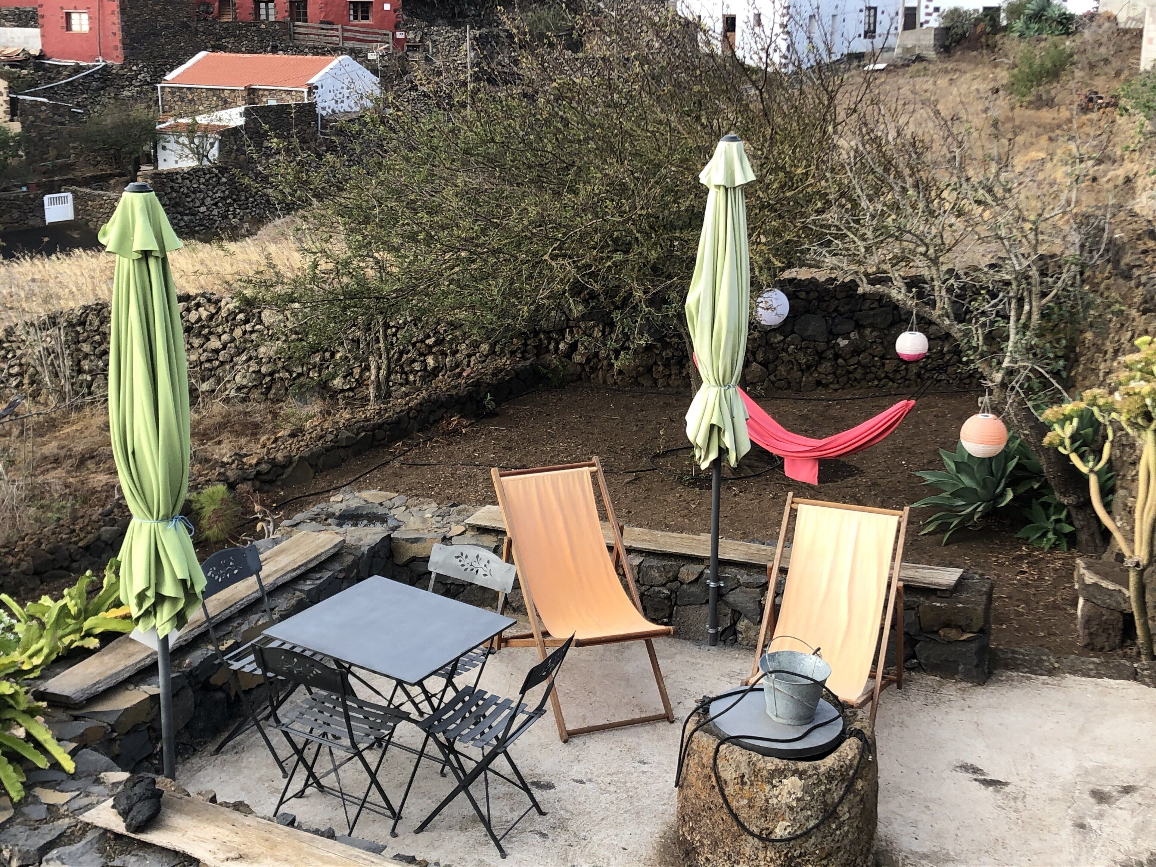 Un espace extérieur aménagé avec des tables et des chaises en métal, des parasols verts et un hamac.