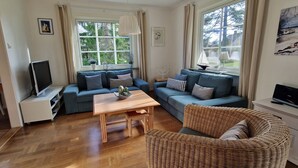 Una sala acogedora con un sofá, un sillón de mimbre, una mesa de madera y un televisor.