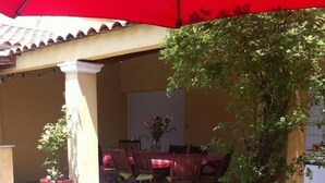 An outdoor patio with a table and chairs, a red umbrella, and a potted plant.