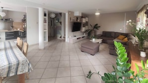 A modern living room with a flat-screen TV, a sofa, and a dining area with a table and chairs.