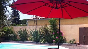 A poolside area with wicker furniture, a red umbrella, and a tiled wall.