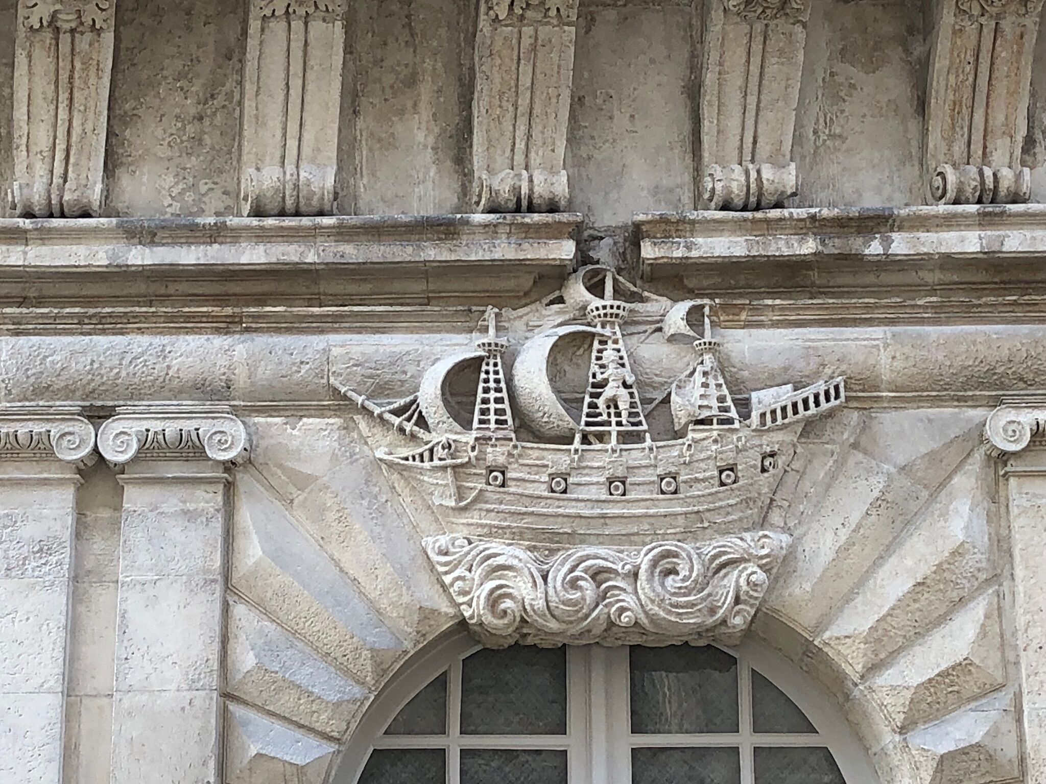 A stone facade with a decorative ship motif above a window.