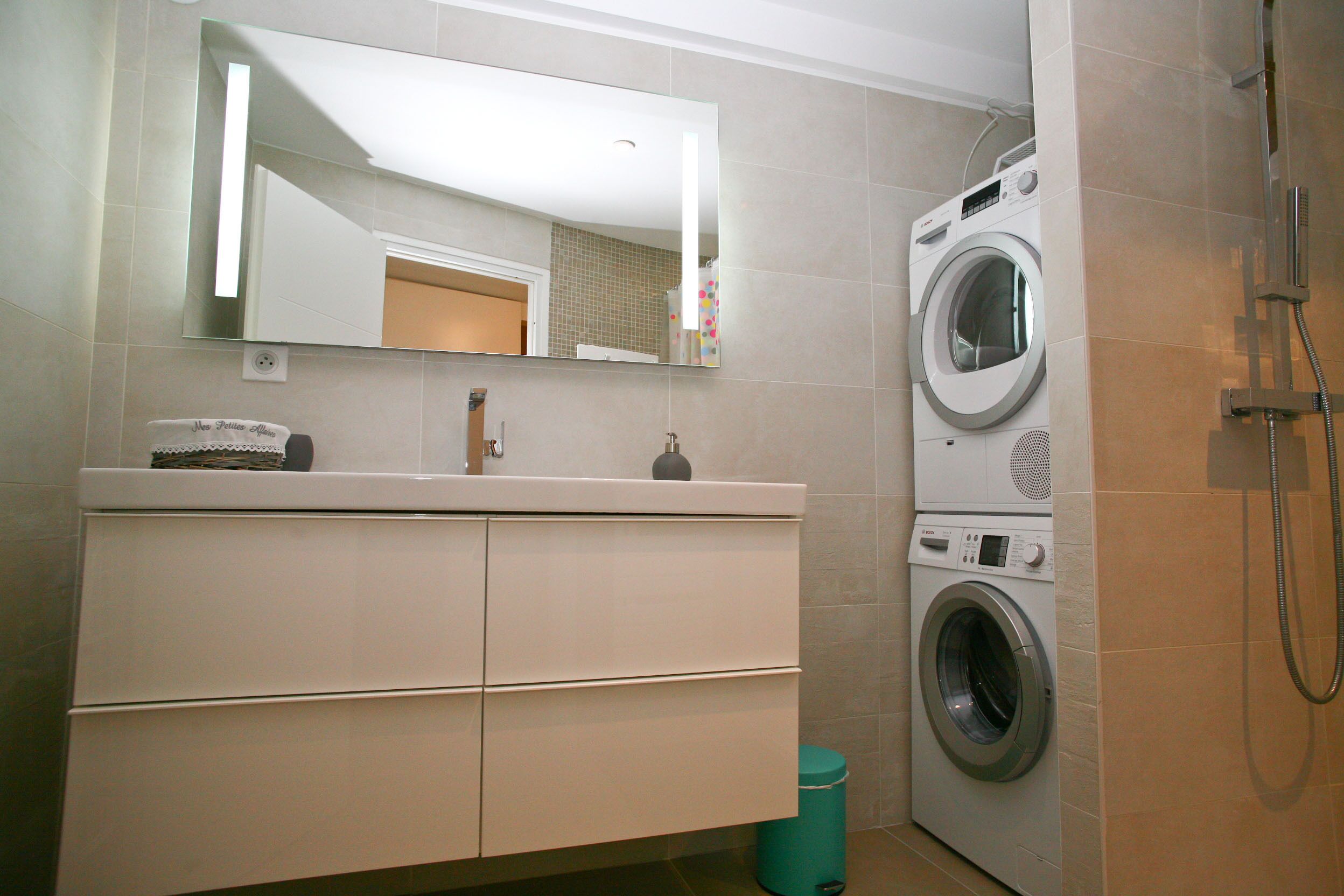 Un bagno moderno con lavatrice integrata, uno specchio grande e una doccia.